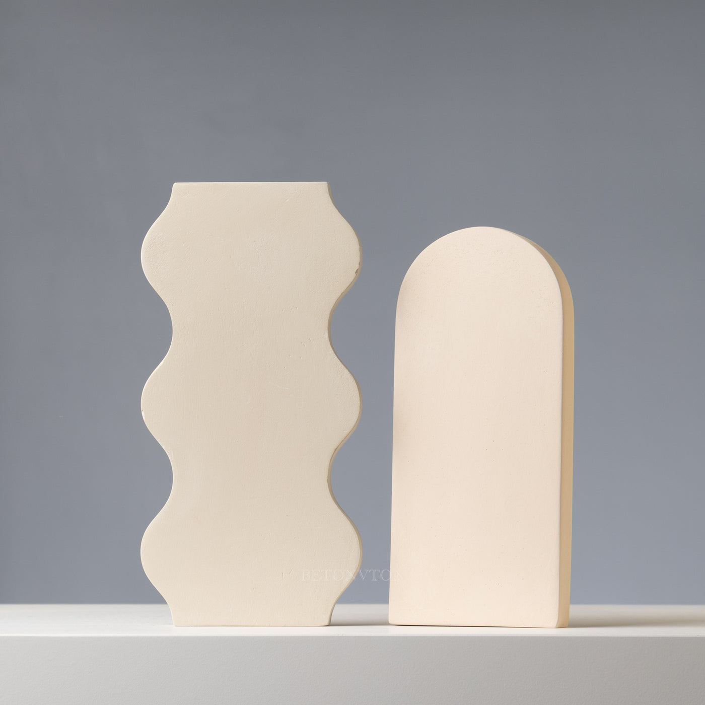 Two beige concrete bookends with wavy design on a gray background